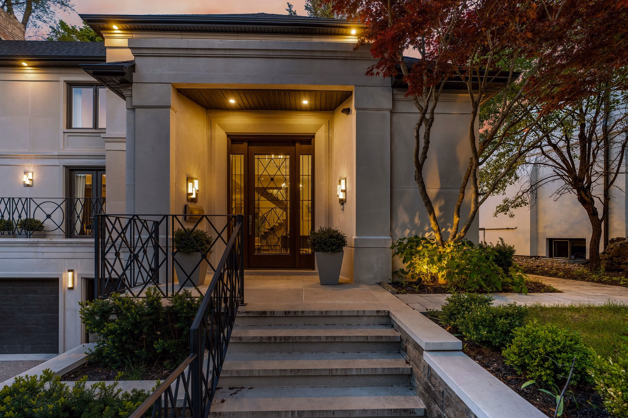 Grand front entrance with stone steps, planters and lantern light at dusk