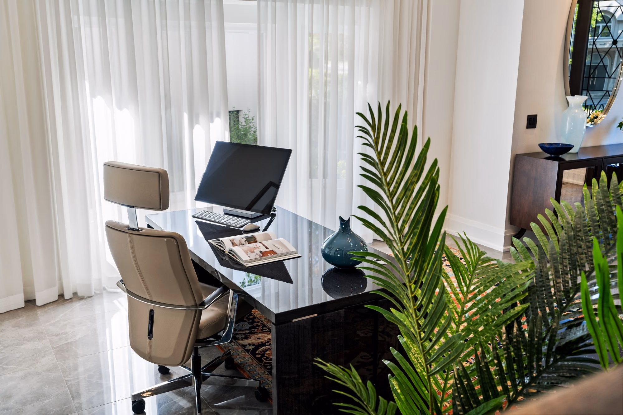 Desk and leather chair by sheer curtains in a home office
