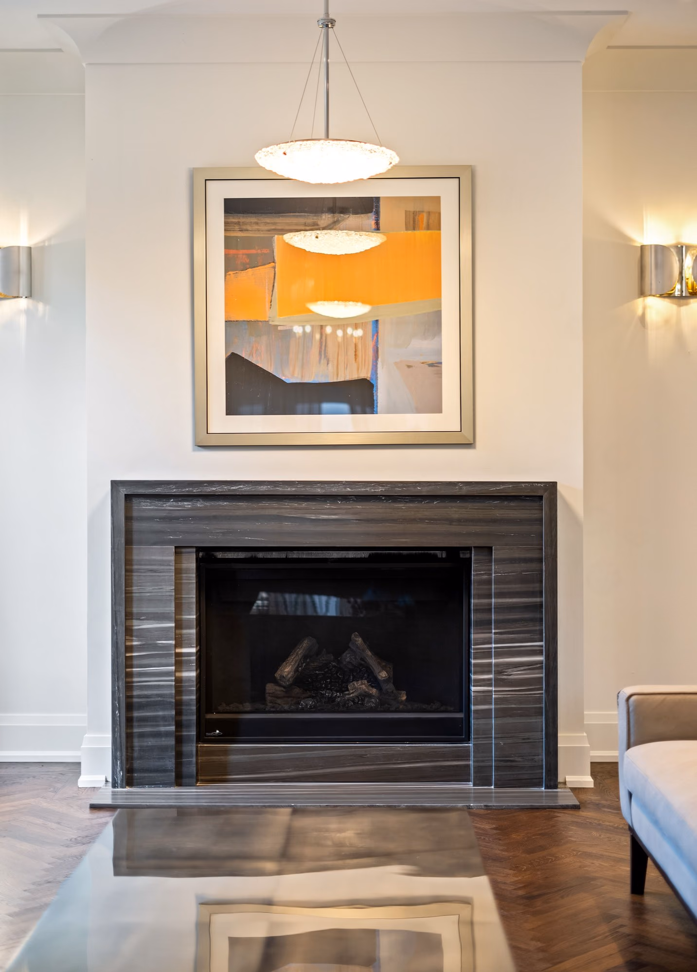 Marble fireplace with abstract artwork, wall sconces and a pendant light