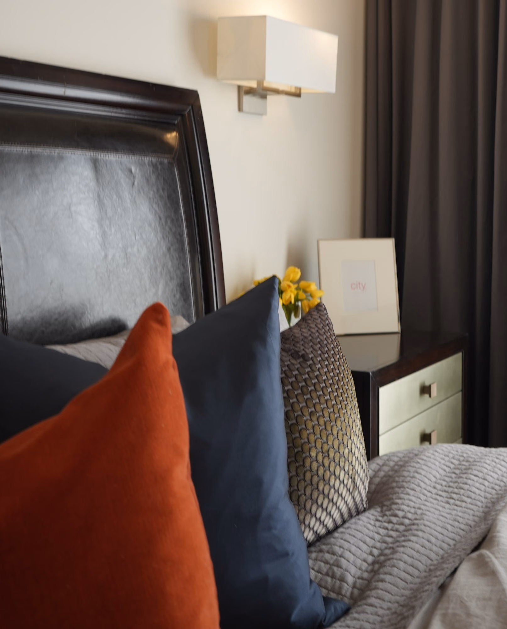 Bedroom detail with leather headboard, sconce and orange cushion