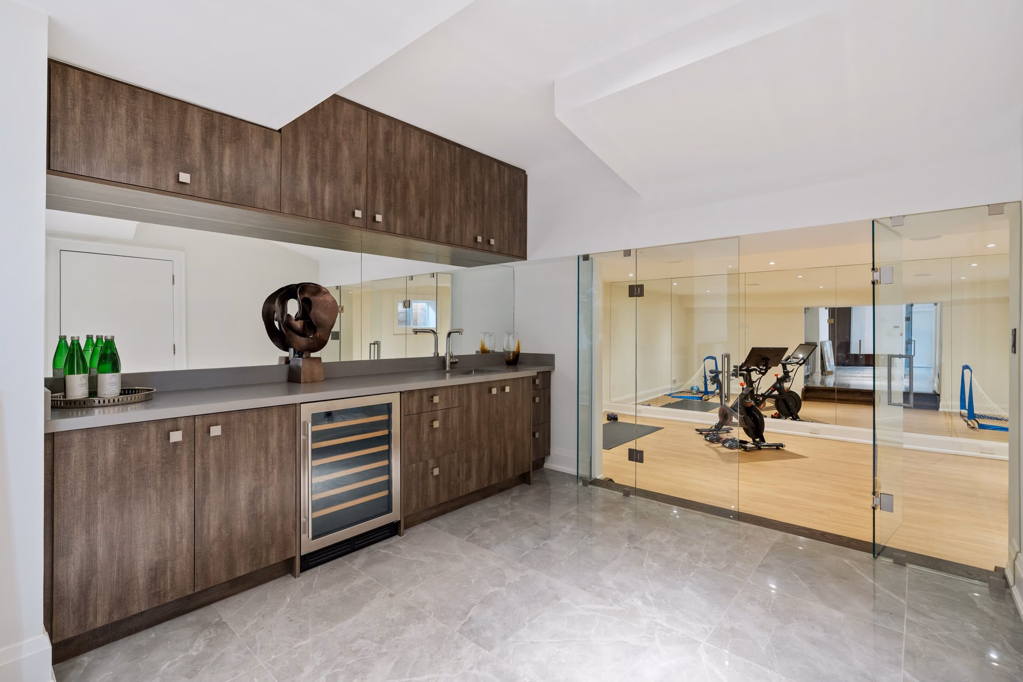 Lower-level bar with wine fridge beside a mirrored home gym