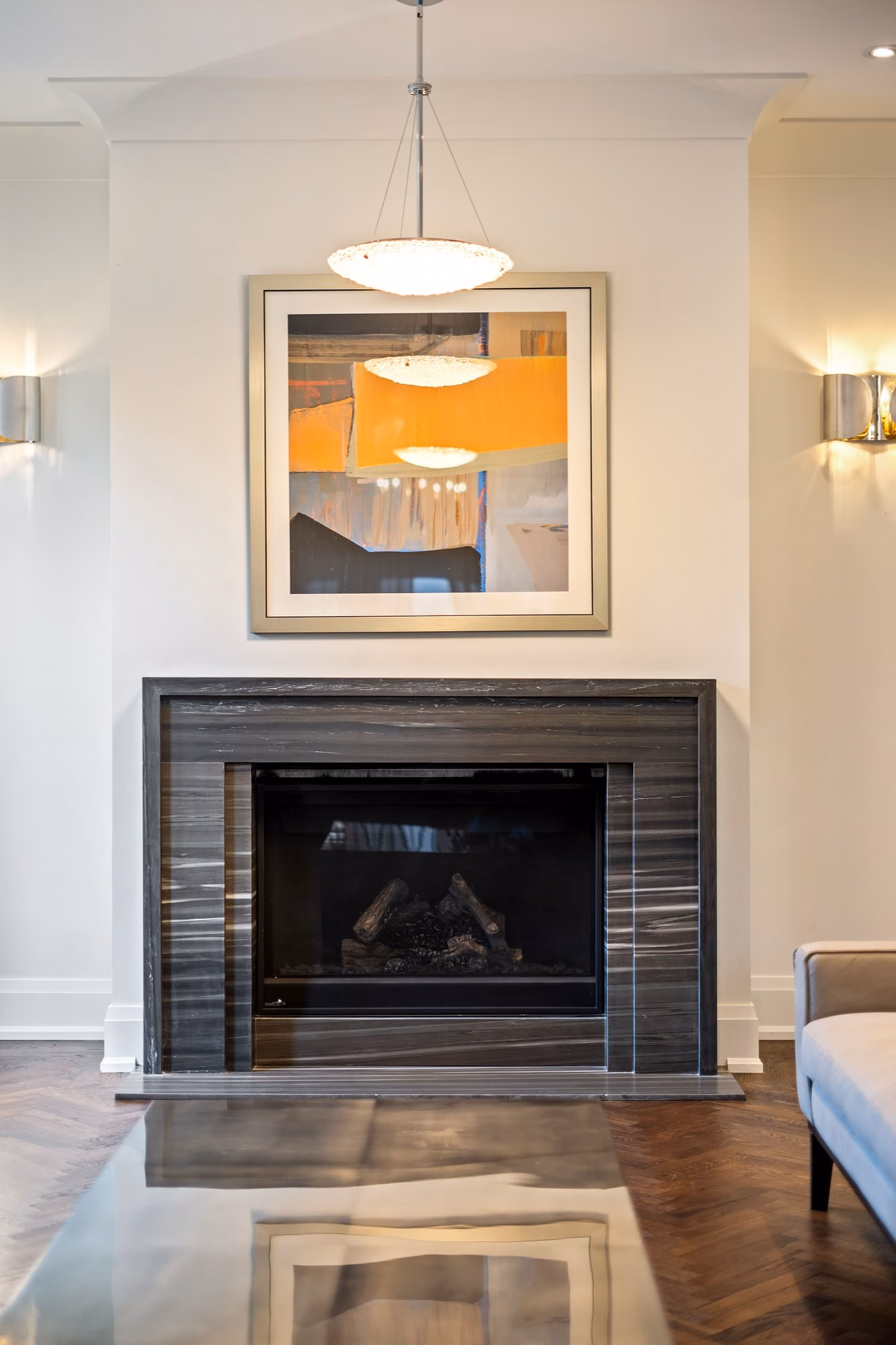 Marble fireplace with abstract artwork, wall sconces and a pendant light